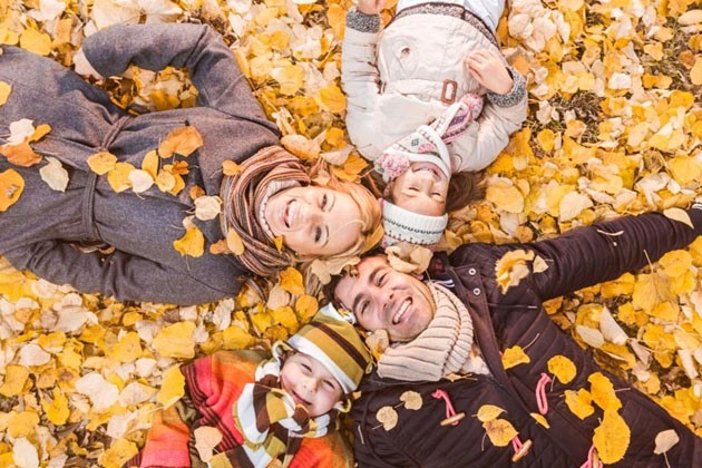 2 adults and 2 kids in winter coats, lying on a pile of fall leaves