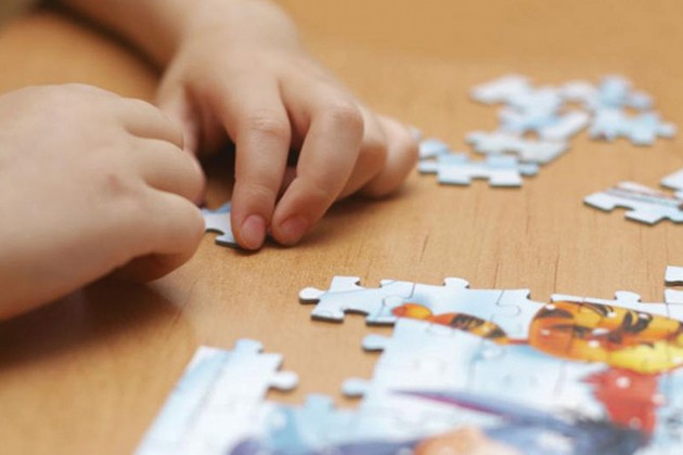 A child’s hands putting puzzle pieces together on a table.