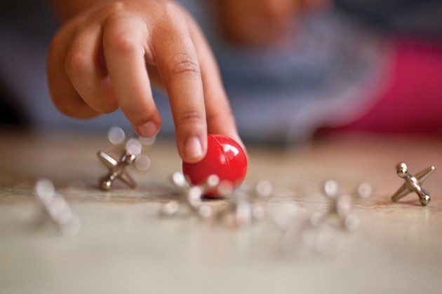 Detské prsty, ktoré drží gumovú guľu blízko zdvihákov na stole