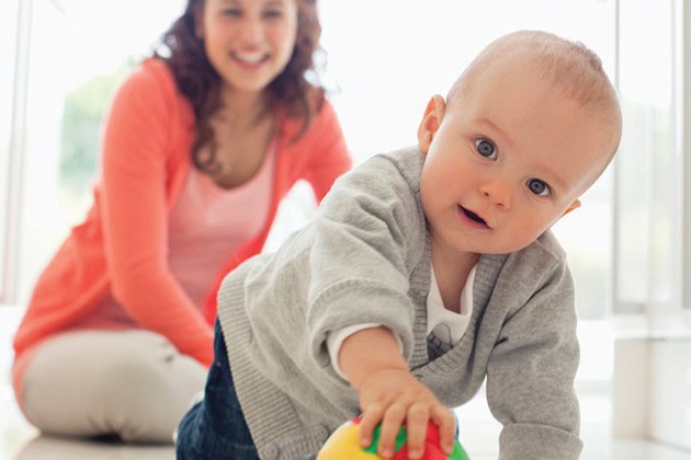 Baby crawling on the floor with a toy while a woman watches.