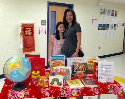 An adult and a child standing behind a table of books about China and some written in Chinese.