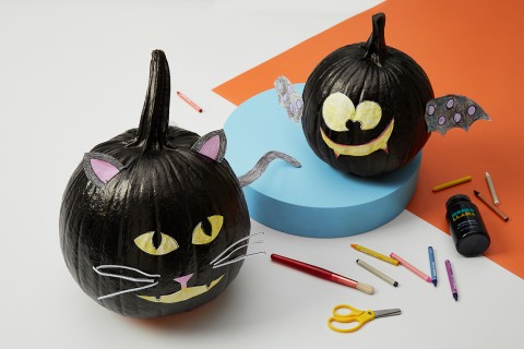 Two black-painted pumpkins, one with a cat design and one with a bat.